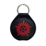 A round, black coin holder with a key ring at the top. In the center is a red embossed image of a the anti-possession symbol.
