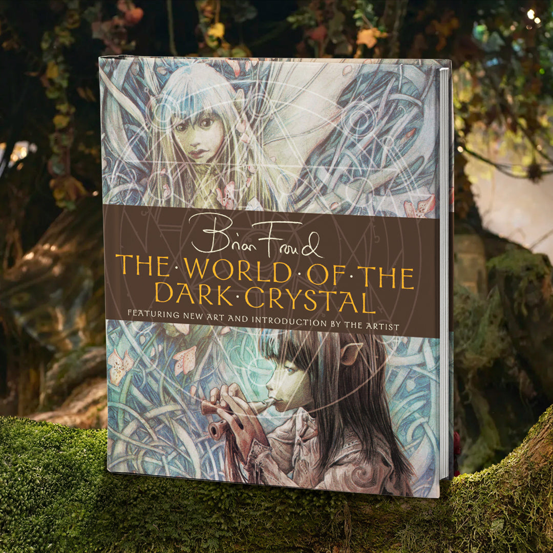 An image of a book cover, with the title "The World Of The Dark Crystal" in yellow text. Behind the text are drawings of two elflike characters from the film "The Dark Crystal, surrounded by grass and flowers. The book is standing on a moss-covered branch, with trees in the background.