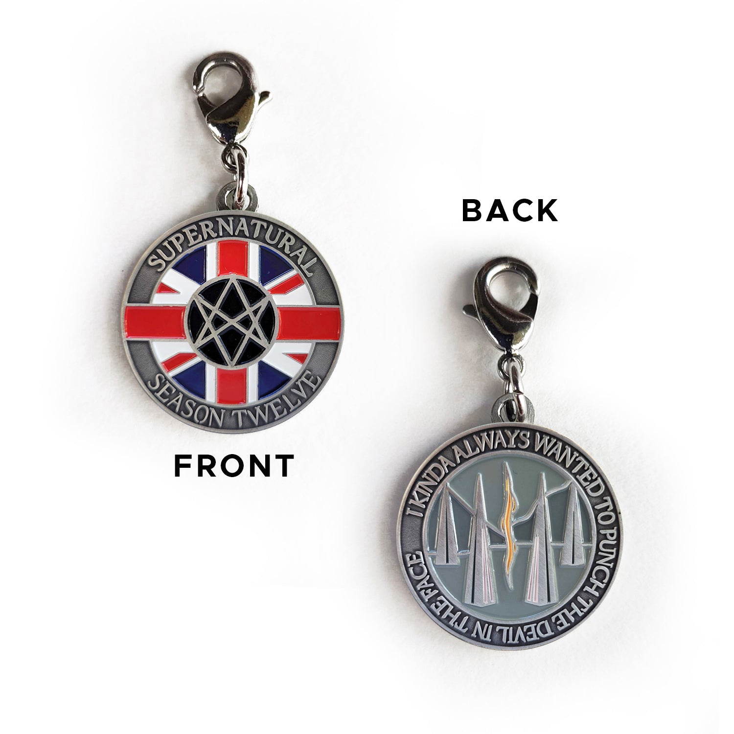 A front and back image of a brass charm. On the front are raised letters around the edge saying “Supernatural season Twelve.” In the middle is a red, white, and blue Union Jack flag, with a Men Of Letters symbol at the center. On the back of the coin are raised letters around the edge saying “I kinda always wanted to punch the devil in the face.” In the middle is are tall triangles rising from a grey background, with a read and yellow line down the center.